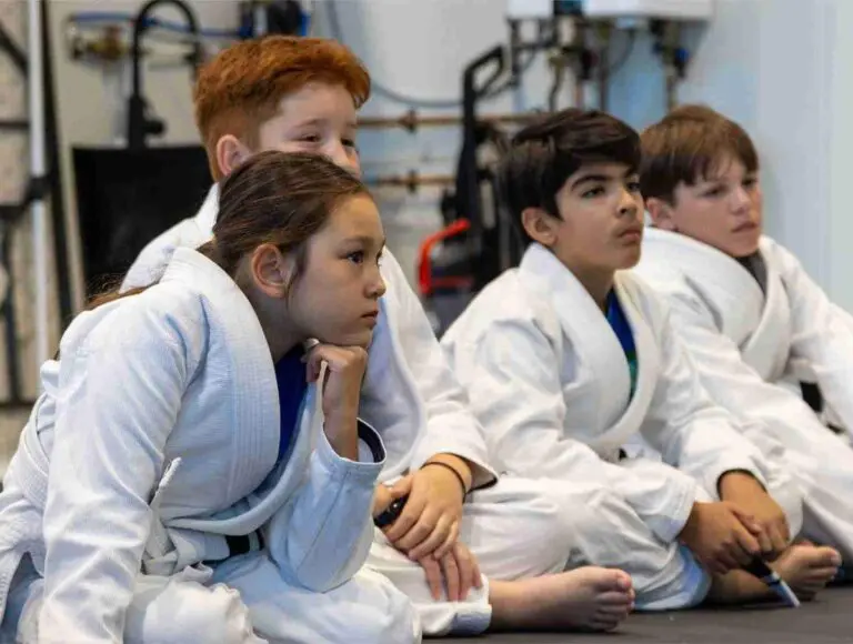 Kids sitting attentively in uniforms while learning awareness and safety principles in a self defense class.