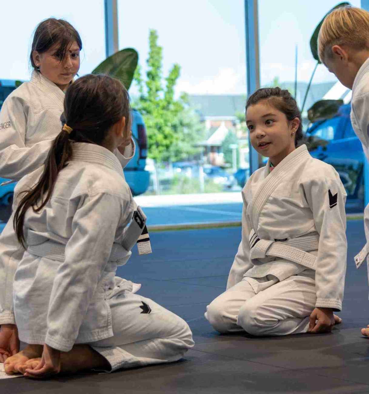 Young students learning practical self defense skills while seated and listening during dojo instruction.
