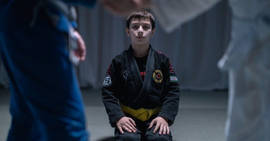 A young boy with a yellow belt sits in a traditional kneeling posture on the mats, focusing on the mental and disciplined aspect of Brazilian Jiu Jitsu Basics.