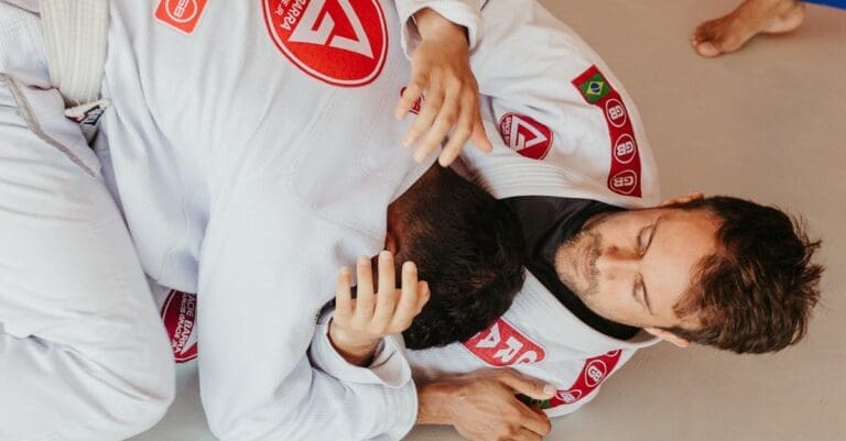 Two adults wearing white Gracie Barra gis practice defensive guard work and transitions, showcasing practical application of Brazilian Jiu Jitsu Basics.