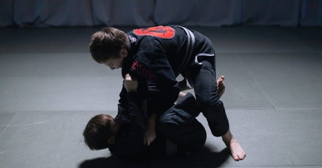 Two young children wearing black gis practice grappling on a mat, demonstrating Brazilian Jiu Jitsu Basics during a training session.