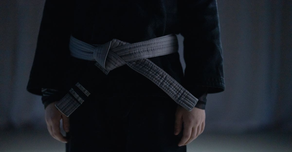 Close-up of a martial artist wearing a black judo gi with a tied white belt around their waist.