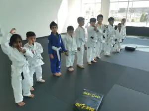 Kids wearing white BJJ gis lining up before class at the academy showing what to wear to BJJ class